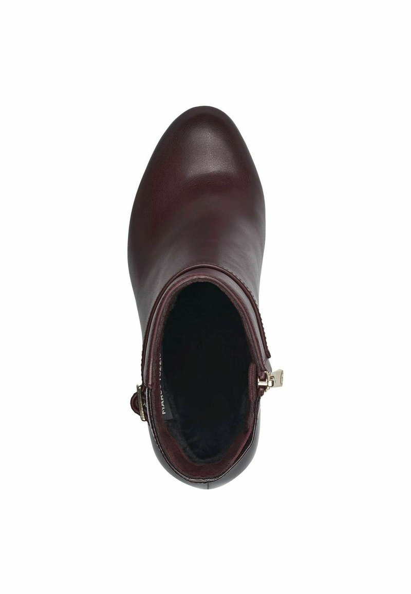 Bottine en cuir bordeaux avec un bout arrondi, fermeture éclair sur le côté et doublure intérieure moelleuse, présentant une texture lisse et un design minimaliste.