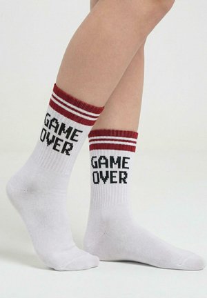 Białe bawełniane skarpety z czerwono-białymi paskowanymi ściągaczami, z napisem „GAME OVER” w czarnej pikselowej czcionce po bokach.