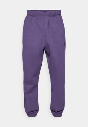 Pantalones de chándal morados con cintura elástica, tobillos acampanados y un pequeño logo negro en el muslo izquierdo. Fabricados con tela suave y transpirable.