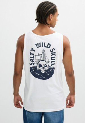 Hombre con el cabello trenzado que lleva una camiseta blanca sin mangas con un gráfico de calavera y barco y el texto "Salty Wild Skull" en la espalda.