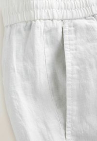 White linen fabric with a textured surface. Features an elastic waistband and side pocket, demonstrating a casual, breathable design.