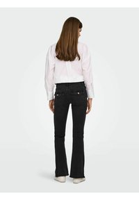 Jeans negros acampanados combinados con una camisa blanca de botones. Los jeans cuentan con bolsillos traseros con detalles de hardware plateado. Textura suave.