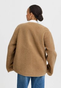 Brun fleecejacka med texturerad yta, oversized design och långa ärmar. Matcher med ljusblå denimjeans.
