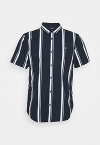 Kortärmad, knappad skjorta i marinblått med vita vertikala ränder. Har en spetsig krage och en liten logotyp på bröstet. Lättviktsmaterial.