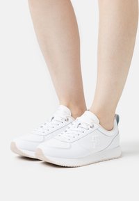 Sneakers bianchi realizzati in materiale sintetico, con una finitura testurizzata, design con lacci e una leggera suola in gomma; logo sul lato.