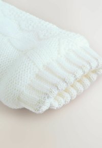 Gestrickter weißer Pulloverärmel mit einem gerippten Bündchen und subtilen metallischen Fäden, die in den Stoff eingewebt sind für zusätzliche Textur.
