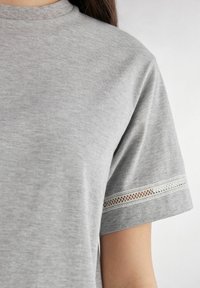 Grijze katoenen t-shirt met een ronde halslijn; korte mouwen met een witte kantafwerking langs de zoom. Glad oppervlak, casual ontwerp.