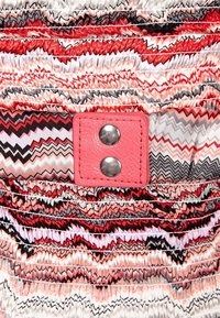 Multikleurige stof met zigzagpatronen in rood, zwart en wit, met een textuur van een roze leren patch en twee zilveren studs.
