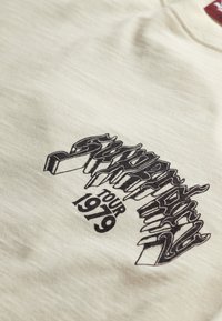 Light beige cotton t-shirt featuring black graphic text that reads "Supertramp Tour 1979" with a stylized design.