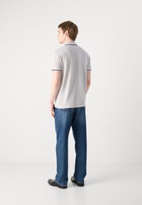 Camisola polo cinza com um acabamento preto, combinada com uns jeans de ganga azuis. A camisola apresenta um colarinho clássico e mangas curtas, exibindo um corte casual.