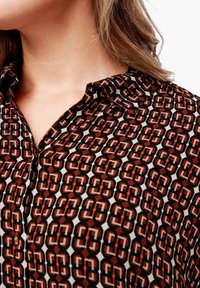Košile na knoflíky s hnědo-bílým geometrickým vzorem, s špičatým límečkem a jemnou, texturovanou tkaninou.
