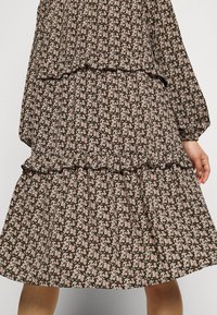 Svart klänning med ett blommönster i rosa och vitt. Har en lagerdesign, volang nertill och långa ärmar, tillverkad av lätt tyg.