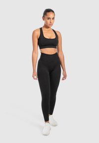 Zwarte sportbeha en hoogopgetrokken leggings van rekbare stof. De outfit heeft een strakke uitstraling met een gladde textuur.