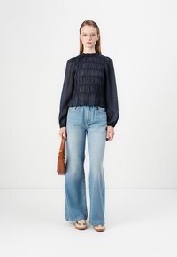 Navy puff-sleeve blouse with gathered texture, paired with light blue flared jeans. Brown handbag and beige shoes complete the outfit.