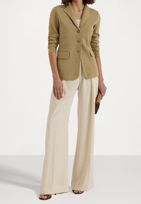 Beige villasekoitteinen bleiseri, jossa on lovettu kaulus, kolme nappia, kaksi etutaskua ja muotonsa mukainen istuvuus, yhdistettynä kermanvärisiin leveälahkeisiin housuihin.