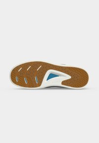 Semelle de chaussure avec une bande de roulement en caoutchouc marron et blanc, motifs géométriques, accents bleus et nom de marque "Clarks" embossé près de la zone de la voûte plantaire.