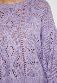 Helllila gestrickter Pullover mit offenen Mustern aus Rauten und Kurven, gerippten Bündchen und einer lockeren Silhouette.