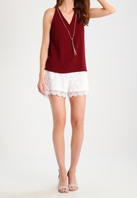 Bordowa bezrękawnik z dekoltem w kształcie litery V, połączona z białymi koronkowymi szortami z falbaną. Uzupełniona jasnoszarymi sandałkami na cienkich paskach.