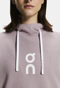 Sudadera con capucha de color lila claro con un gran logotipo blanco, con cordones blancos y una textura suave y lisa.