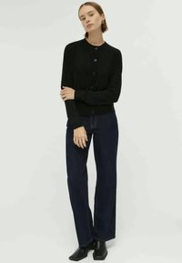 Schwarze Strickjacke mit Rundhalsausschnitt, langen Ärmeln und vorderem Knopfverschluss. Kombiniert mit dunkelblauen, weit geschnittenen Jeans und schwarzen Stiefeletten.