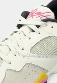 Λευκό αθλητικό παπούτσι με πλέγμα στο πλάι, κρεμ σουέτ λεπτομέρειες, λευκά κορδόνια και μαύρη επένδυση, με ροζ υπογραφή στη γλώσσα και λεπτομέρεια σόλας κίτρινου-ροζ.