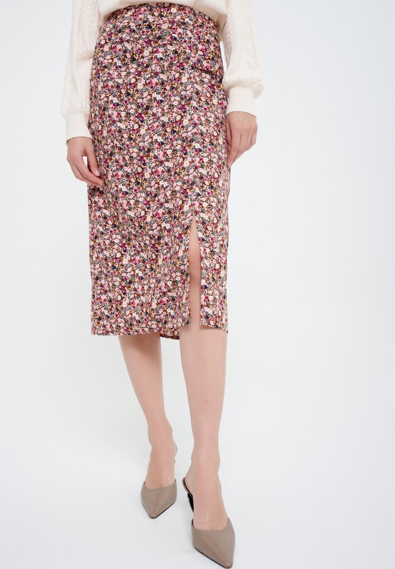 Florale midi-jurk in roze, met verschillende kleine bloemen, een zijsplit en een aangesloten taille. Gedragen met lichtbeige hoge hakken.