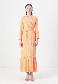 Rochie lungă, stil wrap, dintr-un material texturat de culoare portocalie deschisă. Dispune de un decolteu în V, mâneci lungi și o margine flared cu volane. Se leagă în talie.