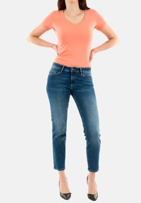 Camiseta de algodón melocotón de manga corta con escote en V, combinada con unos vaqueros ajustados de color azul oscuro. Sus características notables incluyen una cinturilla clásica y un ligero desgaste.