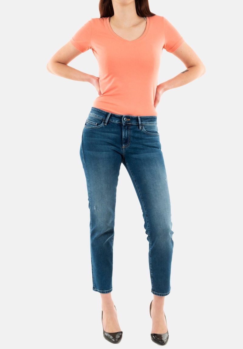 Camiseta de algodón melocotón de manga corta con escote en V, combinada con unos vaqueros ajustados de color azul oscuro. Sus características notables incluyen una cinturilla clásica y un ligero desgaste.