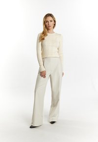 Crème, ribgebreide trui met lange mouwen, gecombineerd met hoge, wijde lichtbeige broek en puntige zwarte schoenen.