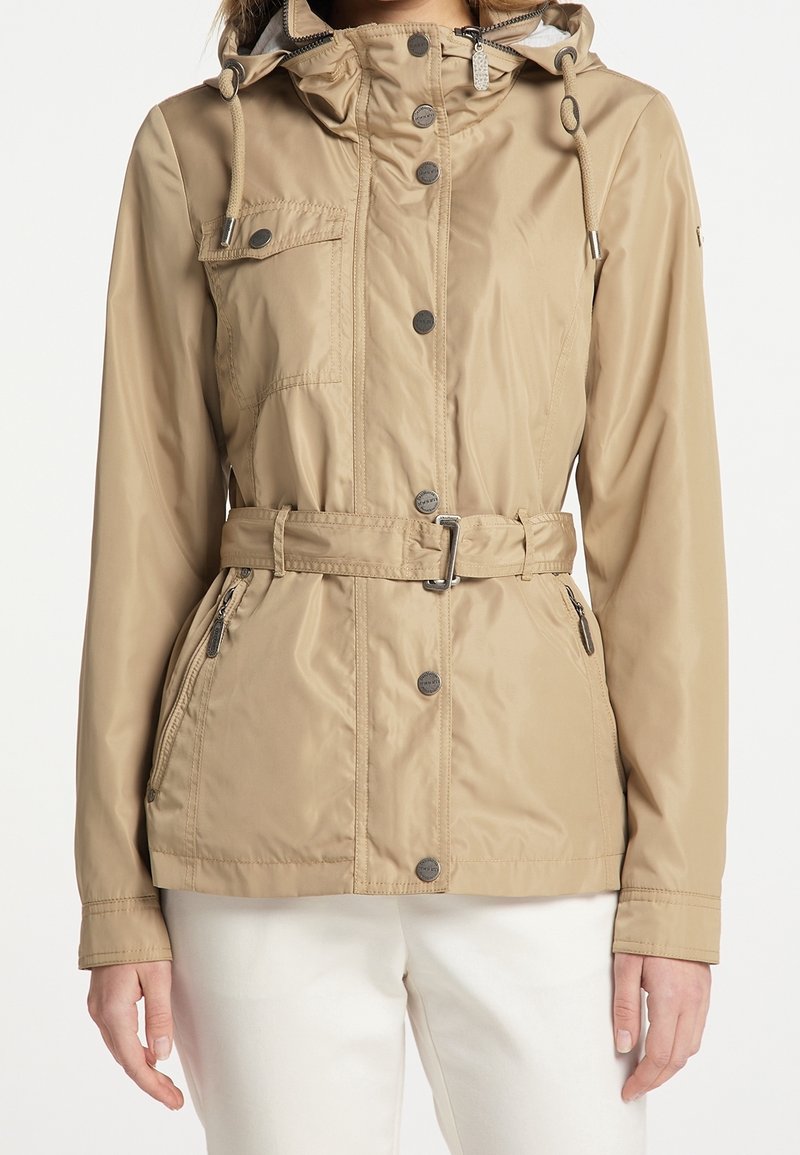 Beige waterdichte jas met een ceintuur in de taille, ritszakken aan de zijkant, knoopsluiting en een verstelbare capuchon met trekkoorden. Gladde textuur.