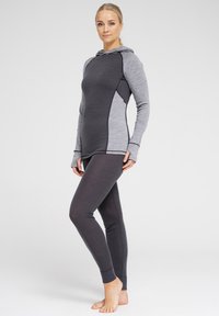 Grå atletisk top med hætte og lange ærmer, med kontrasterende lysegrå paneler. Kombineret med mørkegrå leggings, begge tætsiddende og glatte.