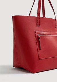 Bolso tote de cuero rojo con asas dobles y un bolsillo exterior frontal con cremallera, mostrado sobre un fondo neutro.