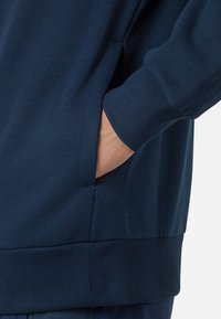 Felpa blu navy con tasca laterale e orlo a coste. Realizzata in tessuto morbido, presenta una vestibilità rilassata e maniche lunghe con polsini a coste.