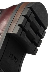Close-up van de zool van een bruine leren schoen met een dikke zwarte rubberen loopzool en een patroon dat grip biedt voor extra tractie.