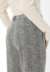 Grijs houndstooth-gepatenteerde broek met een hoge taille, zijzakken en een klein zilveren logoaccent nabij de achterzak. Zachte, gestructureerde stof.