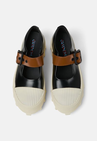 Des chaussures à plateforme noires et crème avec un orteil en caoutchouc texturé blanc, une sangle en cuir marron et un dessus noir lisse. Accentué d'une boucle.