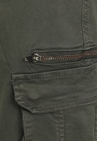 Olivgröna cargo-byxor med en dragkedjeficka, sömdekor och ett mjukt, strukturerat tyg. Utformade för hållbarhet och funktionalitet.
