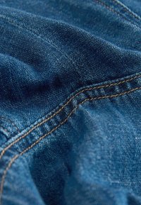 Gros plan sur un tissu en denim bleu avec des coutures marron visibles et un tissage texturé, montrant des plis et des coutures.