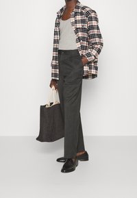 Camicia a quadri con colori rosso, nero e bianco, canotta grigia, pantaloni grigio scuro, mocassini neri e borsa a tracolla nera con texture.