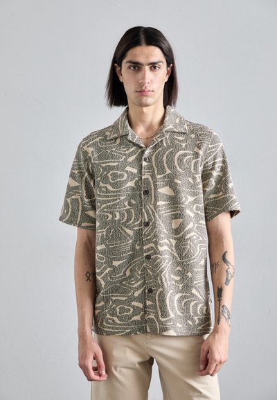 Chemise à manches courtes en beige et marron, avec des motifs abstraits, un devant boutonné et un tissu texturé.