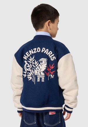 Veste universitaire bleu marine avec manches crème, ornée d'une broderie de tigre et de feuillage dans le dos, poignets côtelés et col rayé.