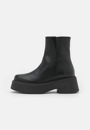 Bottine noire en cuir avec semelle plateforme épaisse et talon bloc, texture lisse et bout légèrement arrondi.