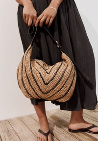 La borsa a tracolla in paglia intrecciata presenta un motivo a spina di pesce con dettagli neri, una forma arrotondata e una tracolla in pelle removibile.