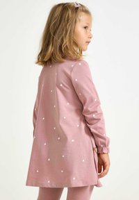 Sukienka z długim rękawem w jasnoróżowym kolorze, wykonana z bawełny, zdobiona białymi kropeczkami, o rozkloszowanym kroju oraz elastycznych mankietach. Ubranie ma boczne rozcięcia.