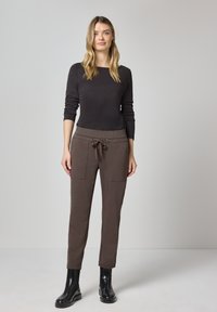 Bruine gebreide broek met een taillekoord, steekzakken aan de voorkant en een slim fit. Gecombineerd met een zwarte top met lange mouwen en zwarte enkellaarzen.