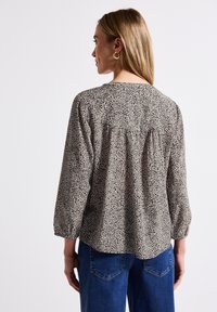 Långärmad skjorta i beige och svart leopardtryck med rynkad detalj bak, tillverkad av lättviktsmaterial. Kombinerad med blå jeans.