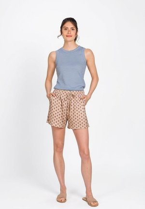 Vrouw staand, gekleed in een blauw gestreept mouwloos topje, beige korte broek met patroon en trekkoord, en beige instapsandalen, tegen een witte achtergrond.