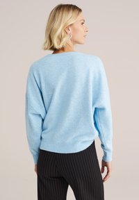 Lichtblauwe trui van zacht, gemêleerd materiaal. Heeft een losse pasvorm, verlaagde schouders en geribde zoom, gecombineerd met zwarte pinstripe broeken.