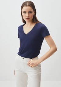 T-shirt blu navy a maniche corte con scollo a V, realizzato in un tessuto morbido, abbinato a pantaloni bianchi a vita alta. Design semplice, senza motivi o accenti visibili.